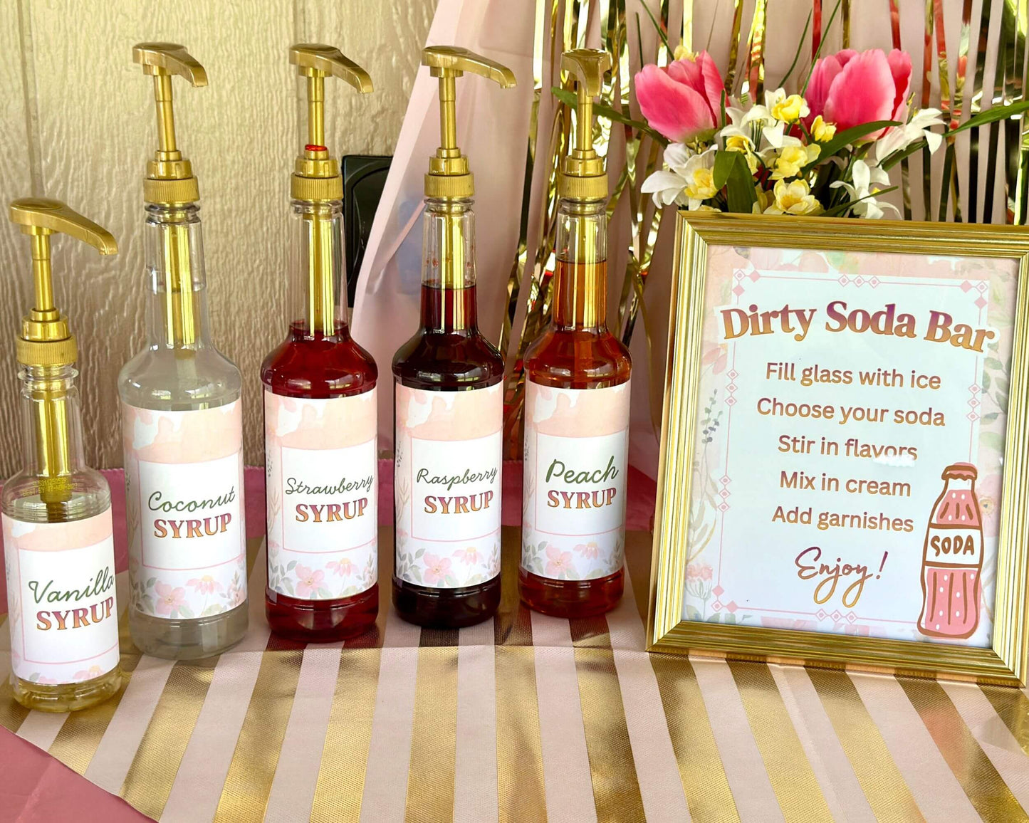 Set of syrup bottles with labels and a 'Dirty Soda Bar' sign on a striped tablecloth.
